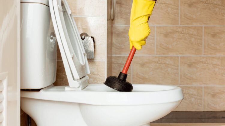 person wearing rubber glove plunging clogged toilet