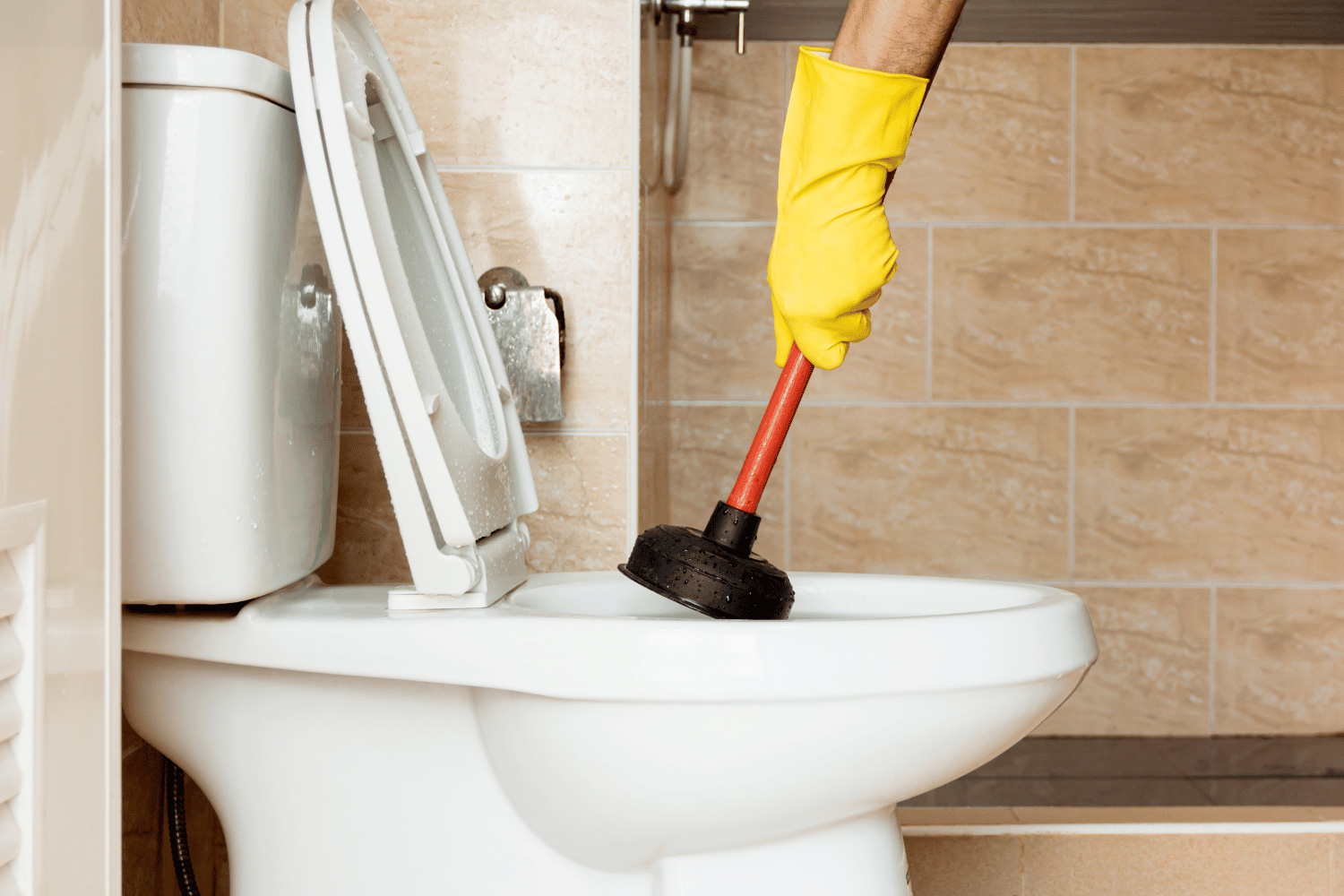 person wearing rubber glove plunging clogged toilet