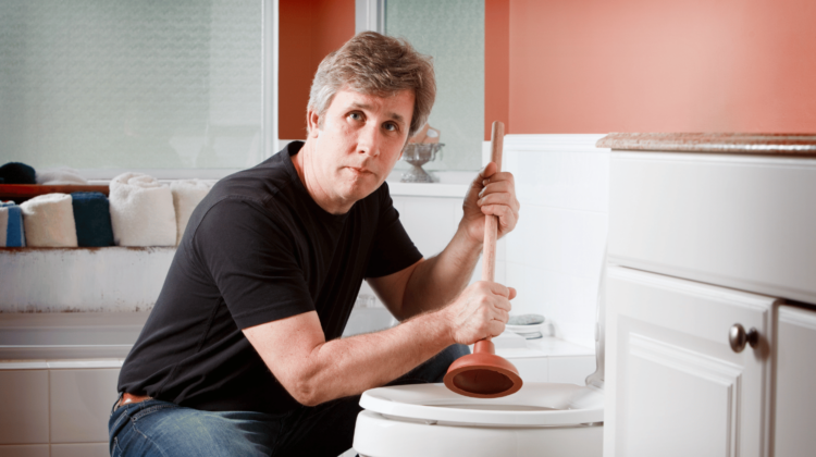 Man using a plunger to clear a clogged toilet in a residential bathroom.