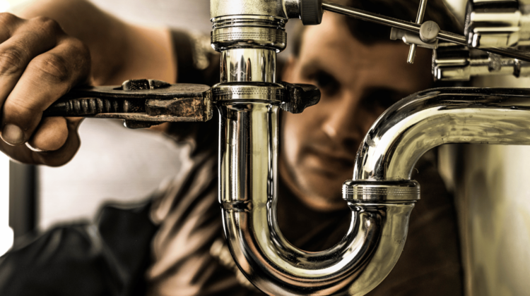Close-up of a plumber using a wrench to tighten a chrome sink P-trap, symbolizing plumbing repair and maintenance.