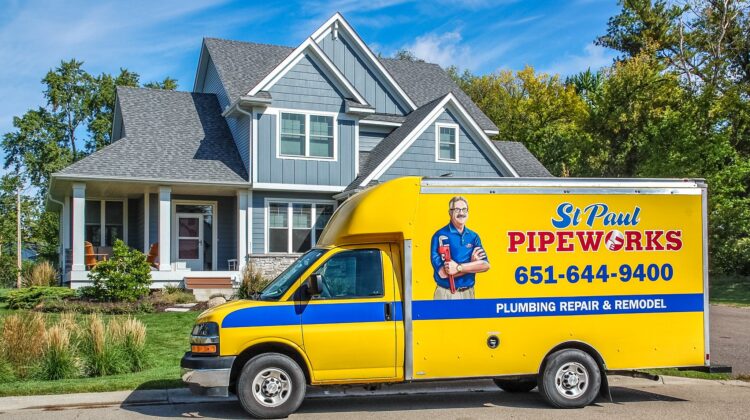 St Paul Pipeworks yellow and blue plumbing service truck parked in front of a modern gray residential home.