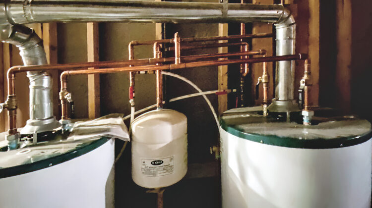 Dual residential water heaters with complex copper piping, galvanized venting ducts, and a thermal expansion tank installed in a utility space.