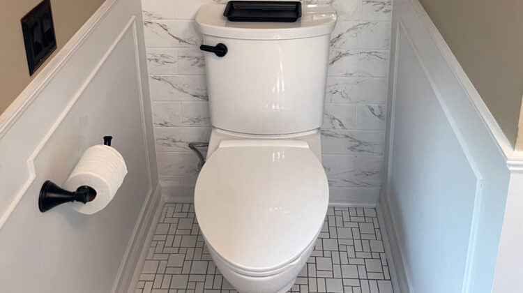 White modern toilet with a comfort-height design, black flush handle, and tiled bathroom floor, installed during a bathroom upgrade by a St. Paul plumber.