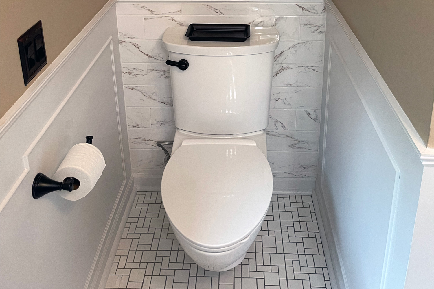 White modern toilet with a comfort-height design, black flush handle, and tiled bathroom floor, installed during a bathroom upgrade by a St. Paul plumber.